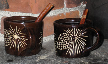 Two mugs of hot rum toddy with cinnamon sticks on top of studio fireplace.  